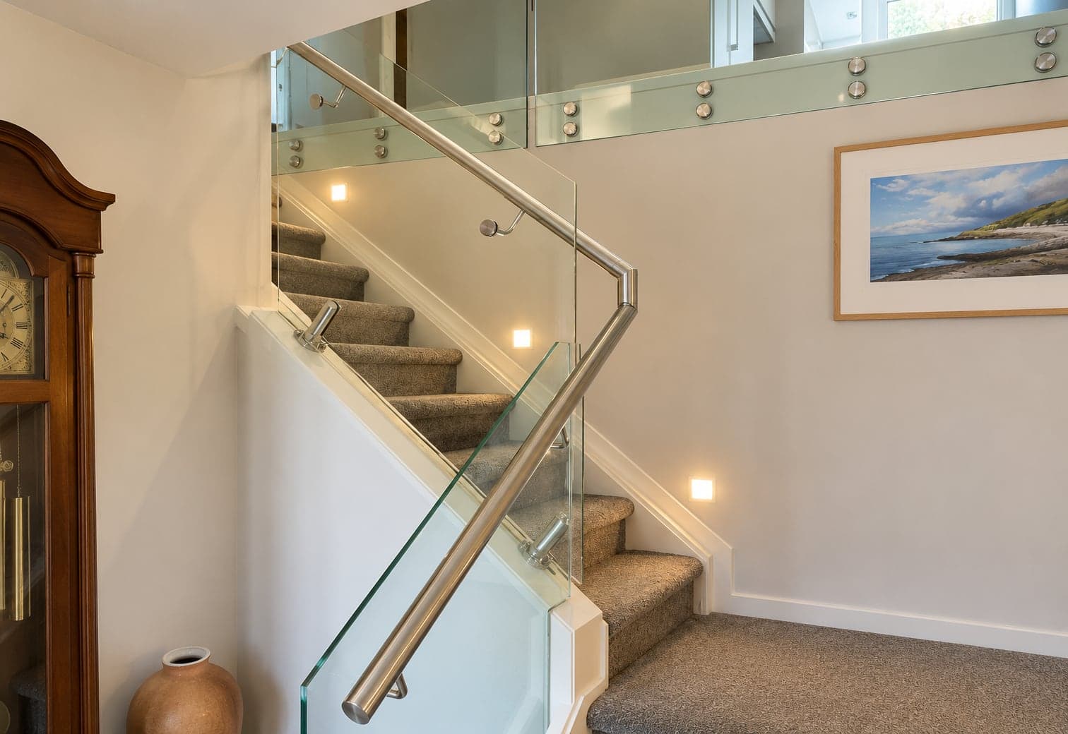 Silver handrail and standoff-mounted glass panels along an indoor staircase