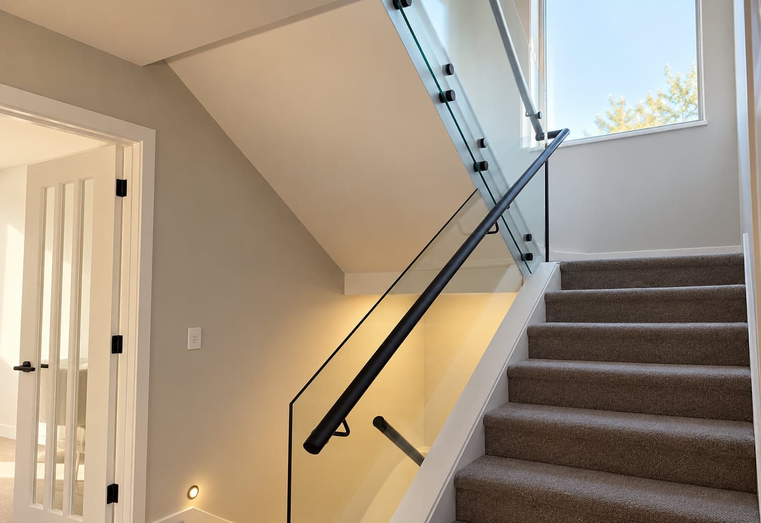 Black handrail fitted beside glass panels and carpeted stairs